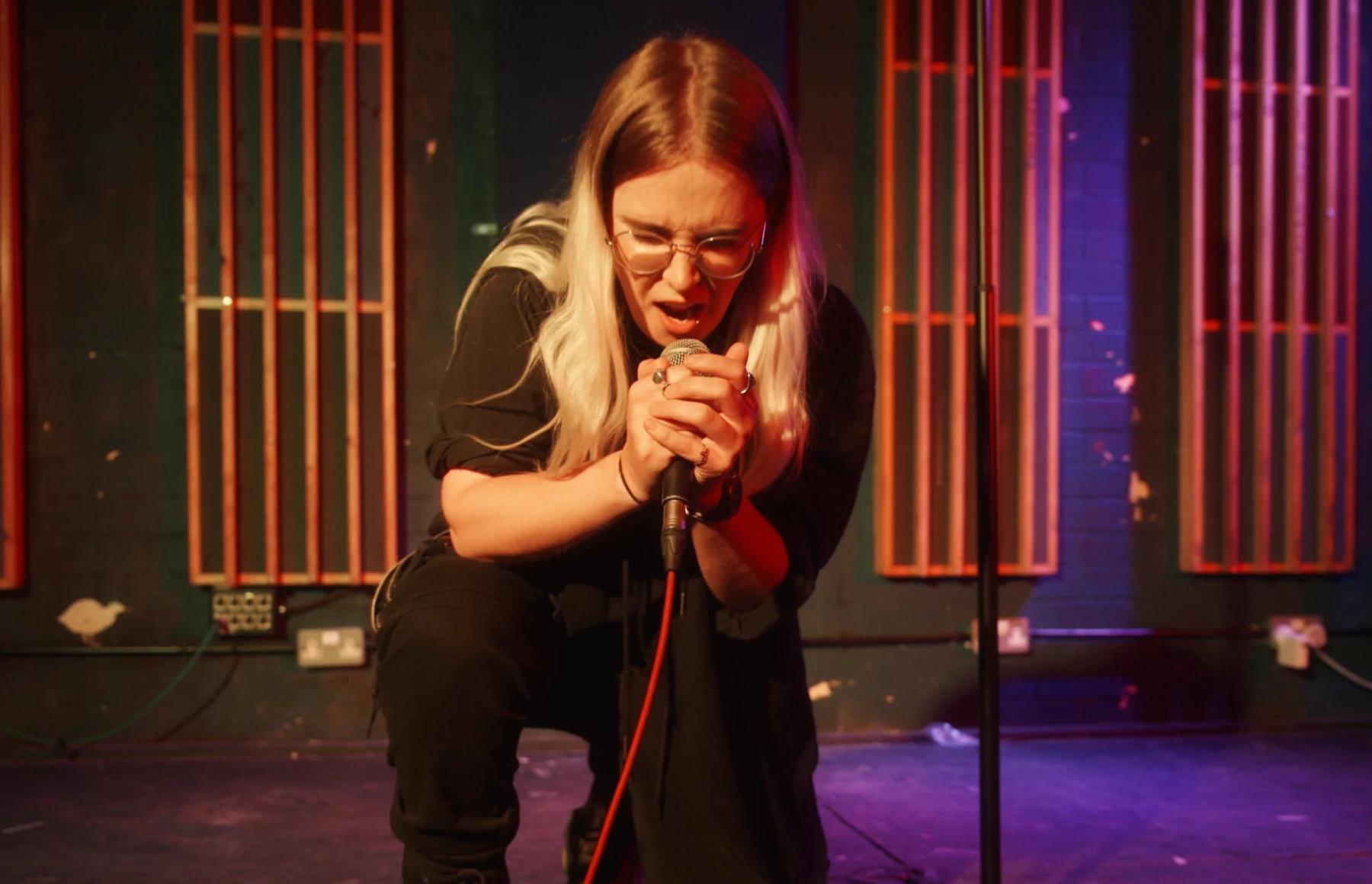 Izzy Kershaw crouched on stage singing into a microphone