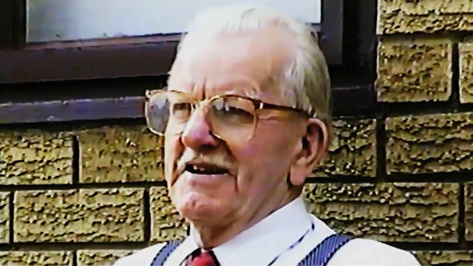 Original VHS portrait of an older man outside a stone building
