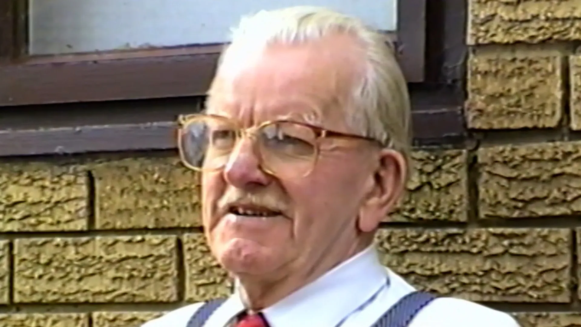 Restored VHS portrait of an older man outside a stone building