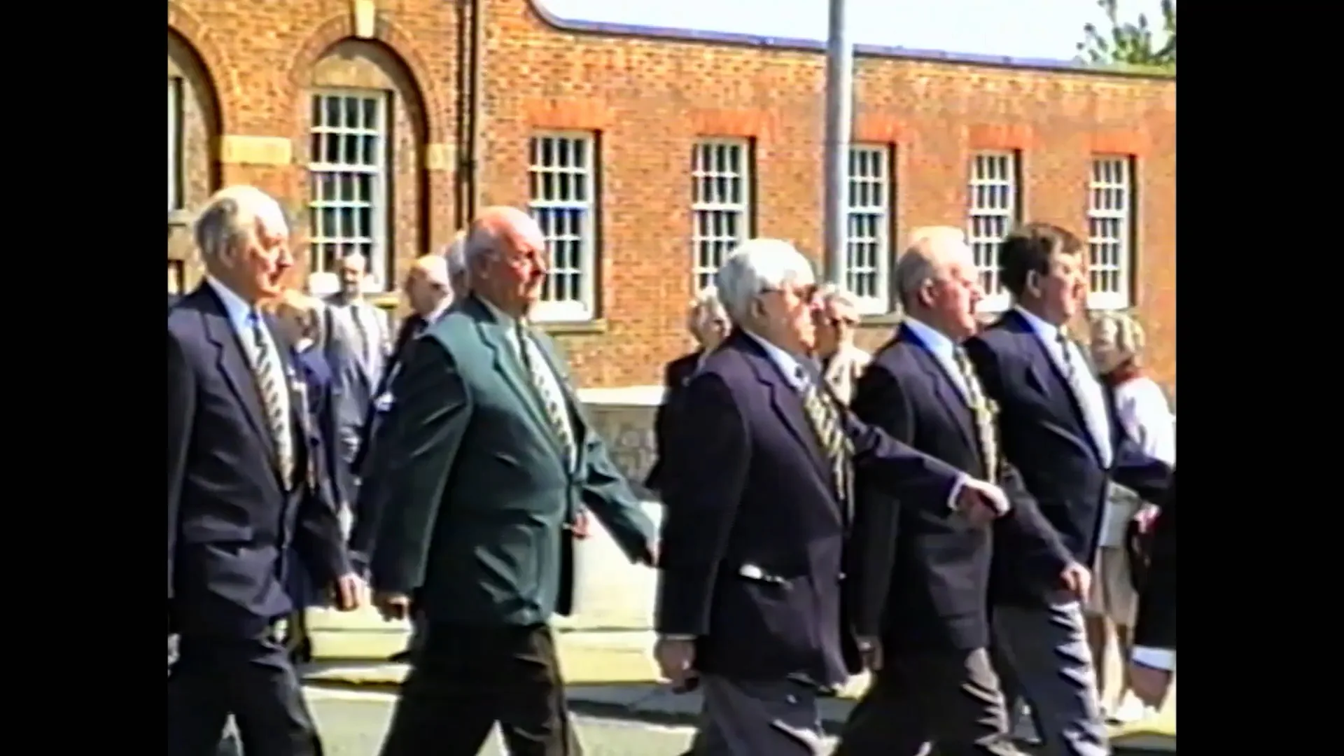 Restored VHS footage of a group walking outside a brick building