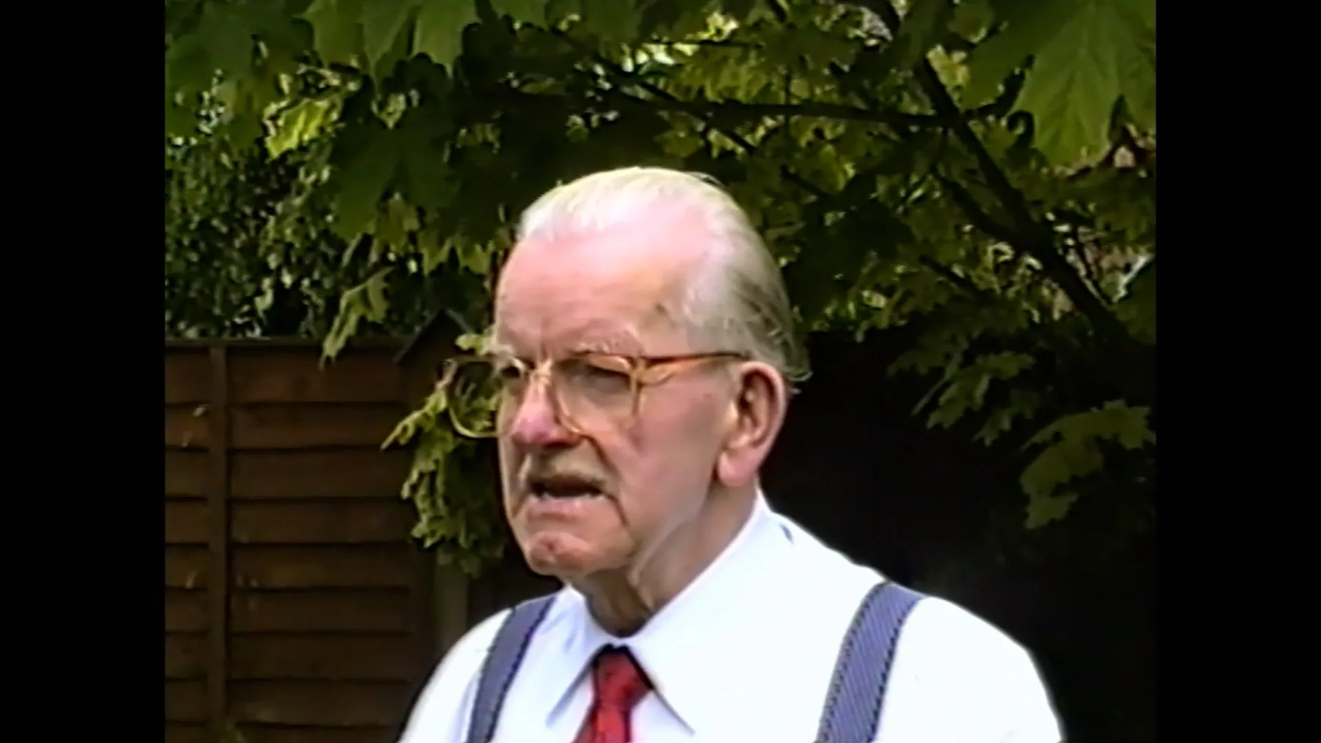 Restored VHS portrait of an older man standing in front of foliage
